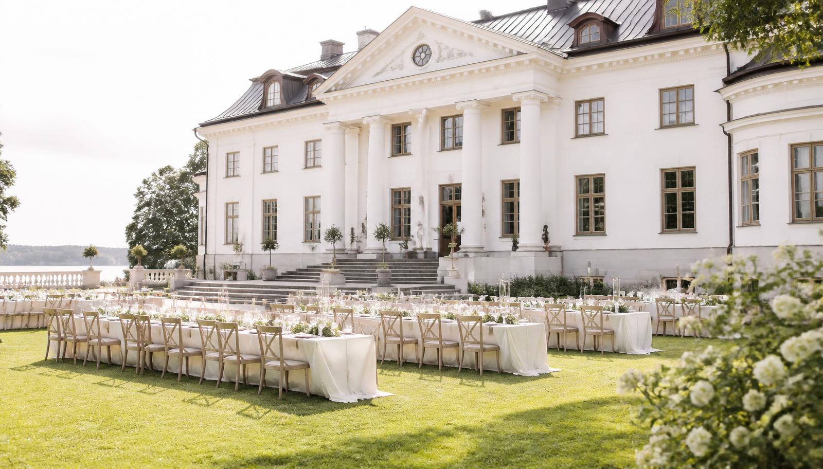 Klassiskt svenskt slott med vita fasader och uppdukat bröllopsmingel på gräsmattan framför huvudbyggnaden.